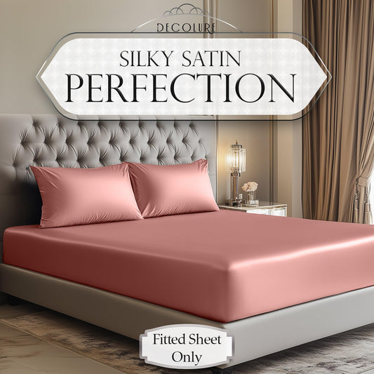 Blush pink satin fitted sheet on a tufted beige upholstered bed with matching satin pillowcases.