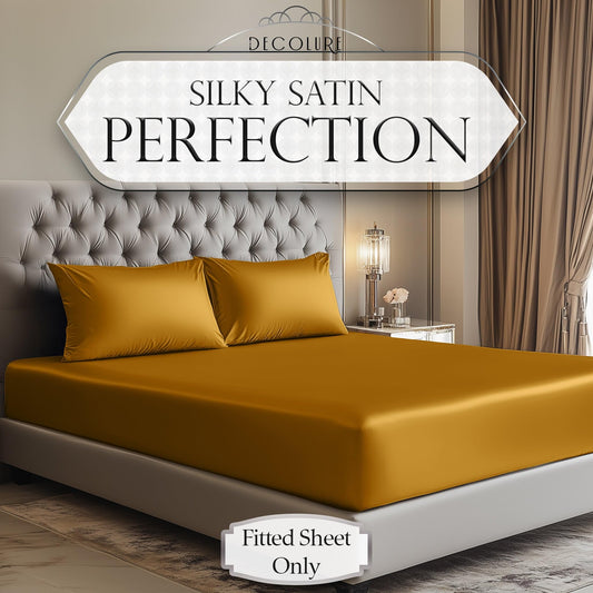 Gold satin fitted sheet with matching pillowcases on a modern tufted bed in a softly lit bedroom.