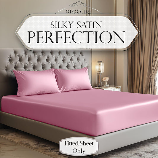 Soft pink satin fitted sheet on king-size bed with matching pillowcases in elegant bedroom.