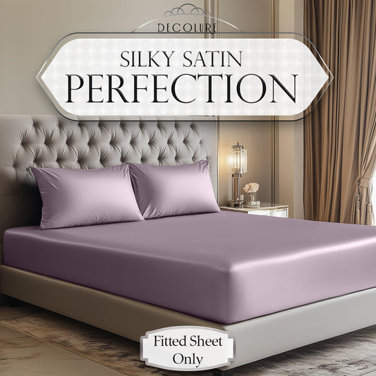 Lavender satin fitted sheet and matching pillowcases on beige tufted bed in neutral bedroom.