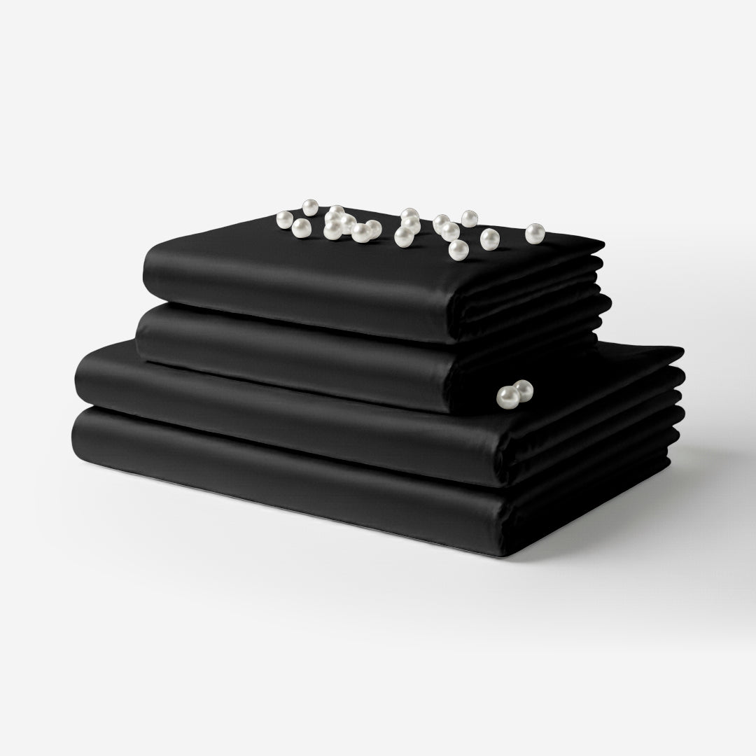 Black satin sheet set neatly folded with a smooth, shiny finish and pearl beads on top.