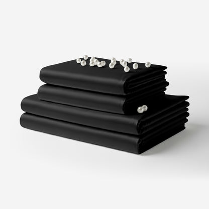 Black satin sheet set neatly folded with a smooth, shiny finish and pearl beads on top.
