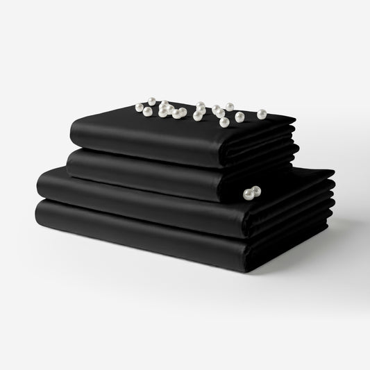 Black satin sheet set neatly folded with a smooth, shiny finish and pearl beads on top.