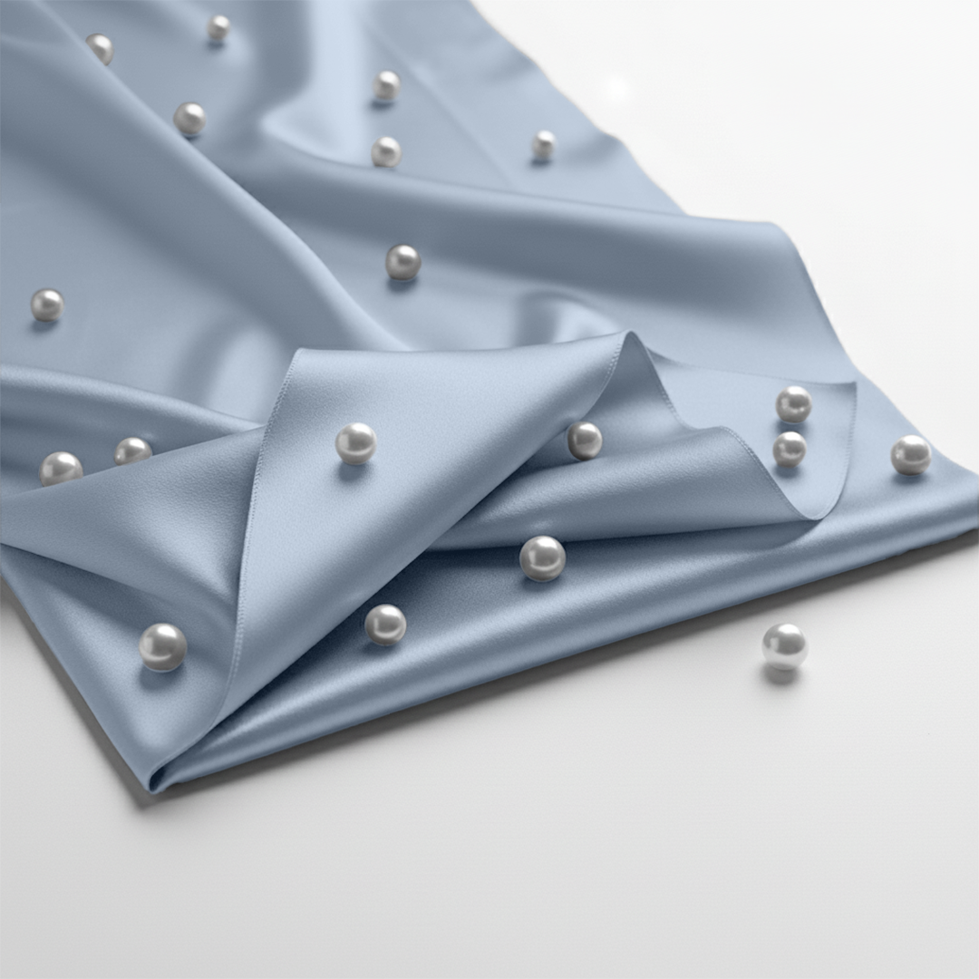 Baby blue satin fitted sheet adorned with scattered small white pearls on smooth fabric.
