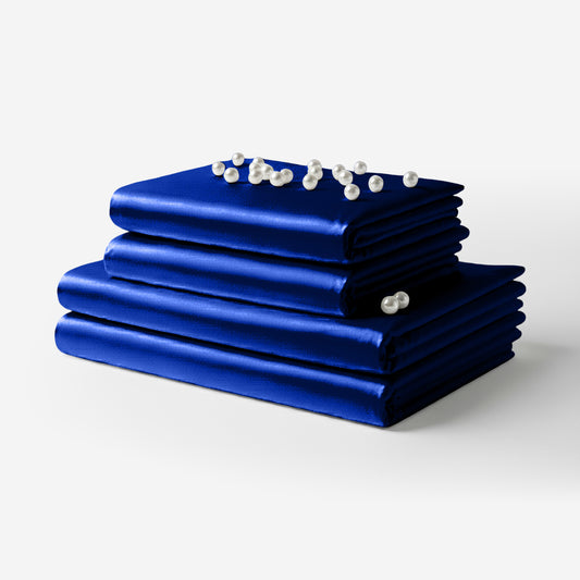 Stack of folded royal blue satin sheets with pearl decoration on top against white background.