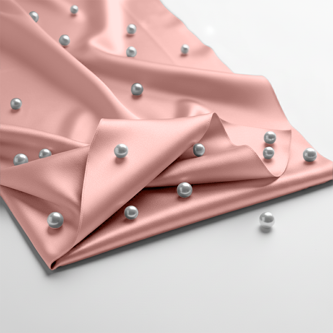 Blush pink satin fitted sheet decorated with scattered silver pearls on smooth fabric surface.