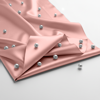 Blush pink satin fitted sheet decorated with scattered silver pearls on smooth fabric surface.