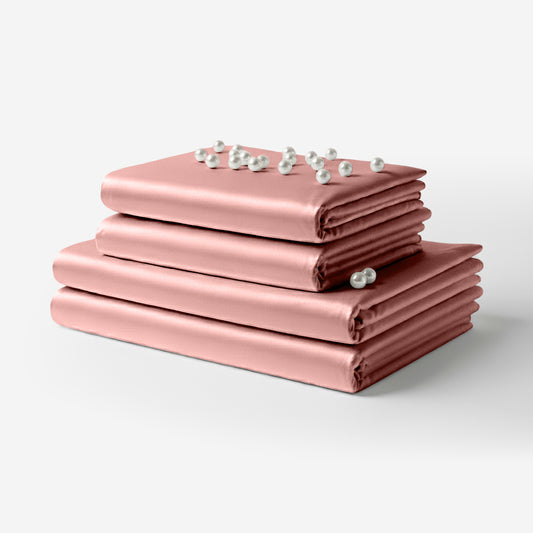 Stacked blush pink satin sheets with a smooth, glossy finish and delicate small white flowers on top.