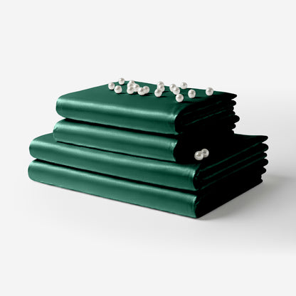 Stack of dark green satin bed sheets with smooth, glossy finish and decorative pearl accents on top.