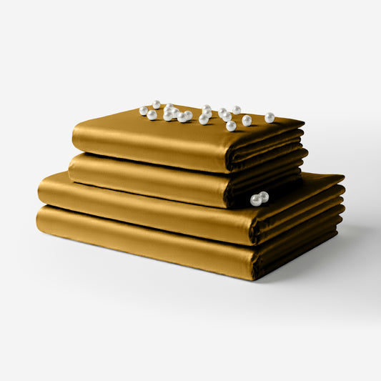 Stack of smooth gold satin sheets neatly folded with a string of white pearl beads on top.