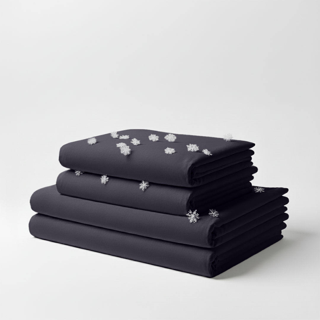 Stacked graphite-colored cooling bed sheets with smooth, wrinkle-free fabric and small white snowflake graphics on top sheet.