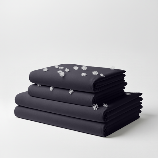 Stacked graphite-colored cooling bed sheets with smooth, wrinkle-free fabric and small white snowflake graphics on top sheet.