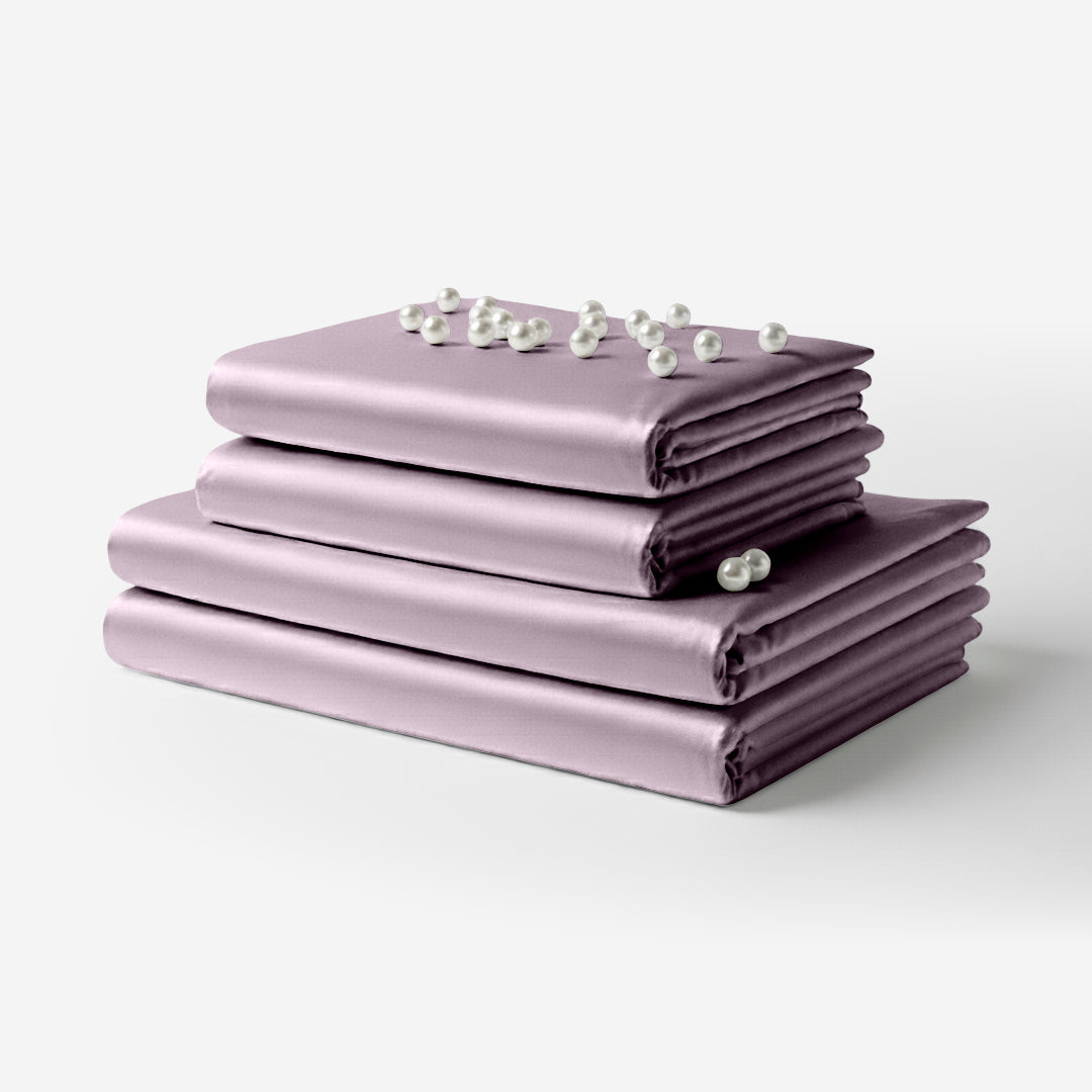 Stack of smooth lavender satin bed sheets neatly folded with small white flowers on top.