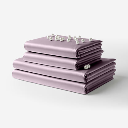 Stack of smooth lavender satin bed sheets neatly folded with small white flowers on top.