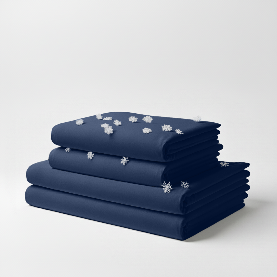 Stack of folded navy blue cooling bed sheets with snowflake icons on top against a white background.