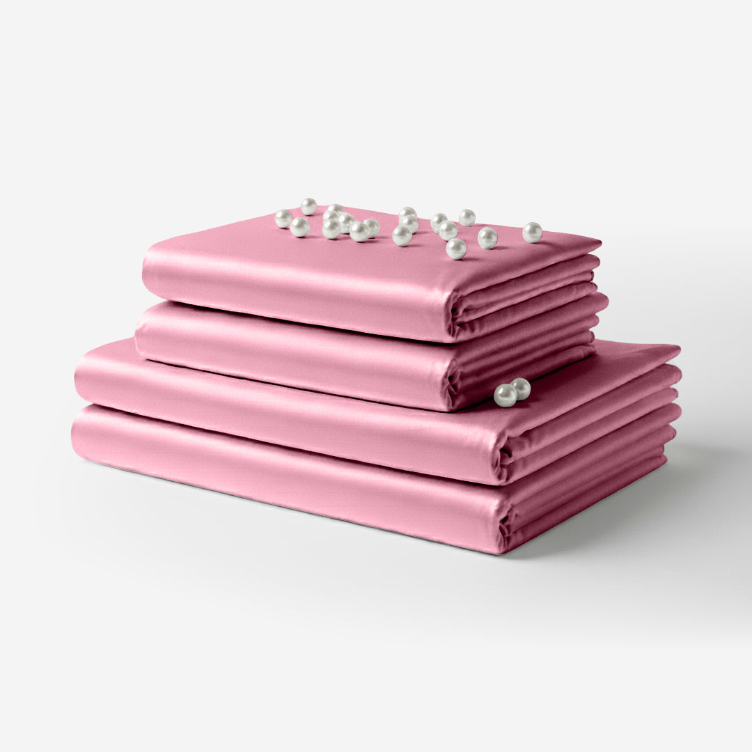 Folded pink satin sheet set with a smooth, glossy finish and delicate white flower accents on top.