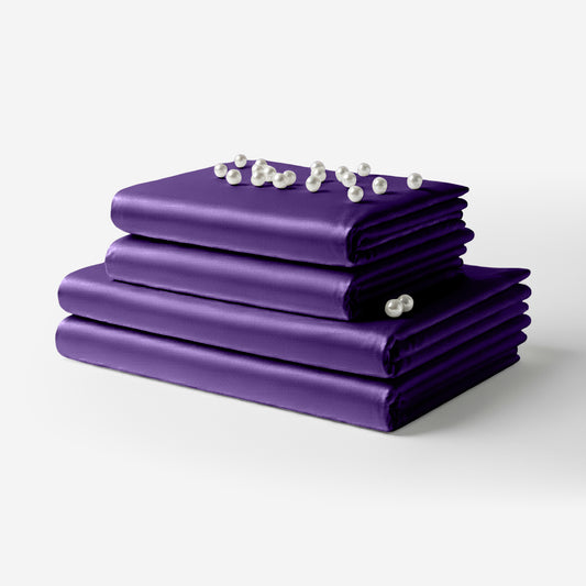 Folded purple satin bed sheet set with smooth, glossy finish and decorative pearls on top.