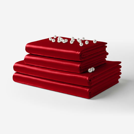 Stack of smooth red satin sheets with a small cluster of white pearls on top.