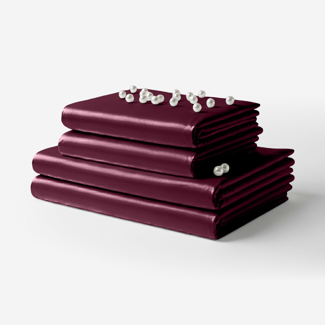 Folded rosewood satin sheet set with smooth, glossy finish and decorative pearl accents on top.