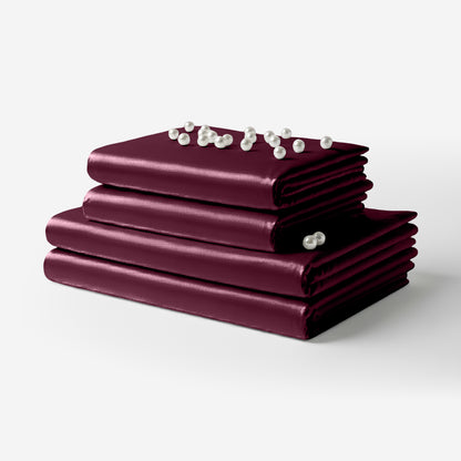 Folded rosewood satin sheet set with smooth, glossy finish and decorative pearl accents on top.