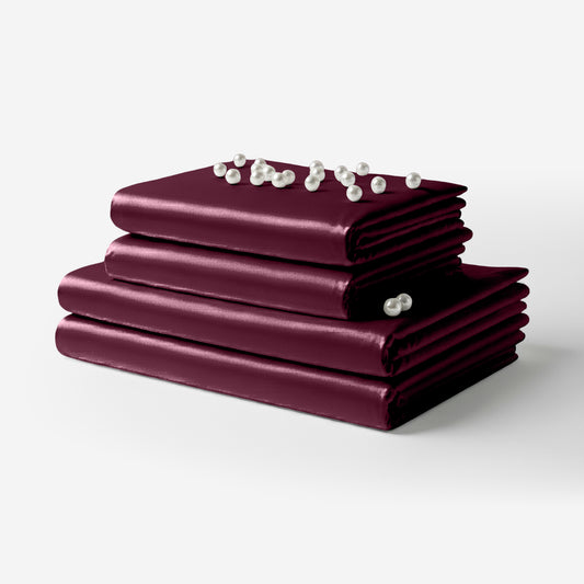 Folded rosewood satin sheet set with smooth, glossy finish and decorative pearl accents on top.