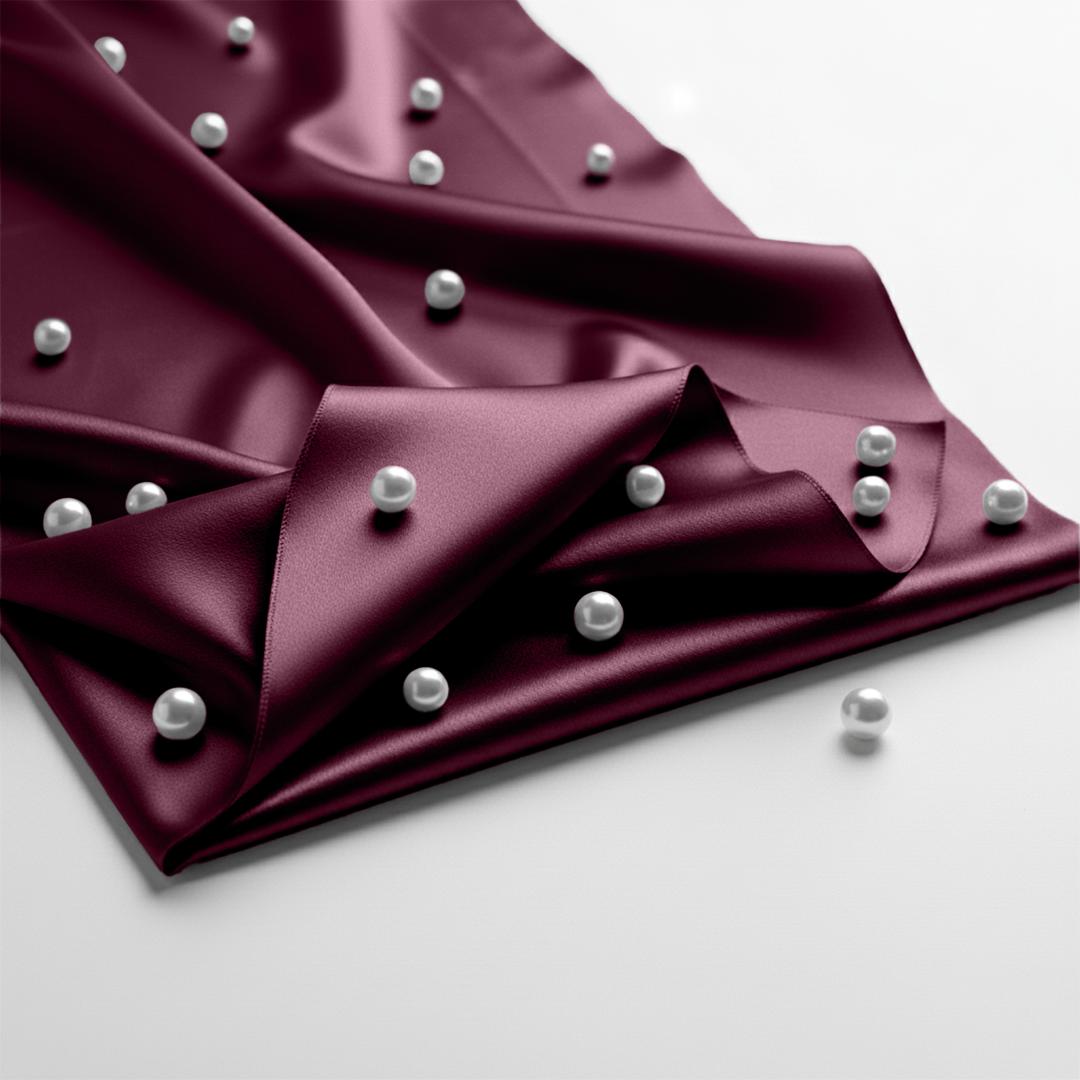 Rosewood satin fitted sheet with smooth texture and scattered white pearls on fabric.