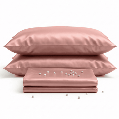 Set of pink satin pillows and a matching sheet with scattered pearls on a white background
