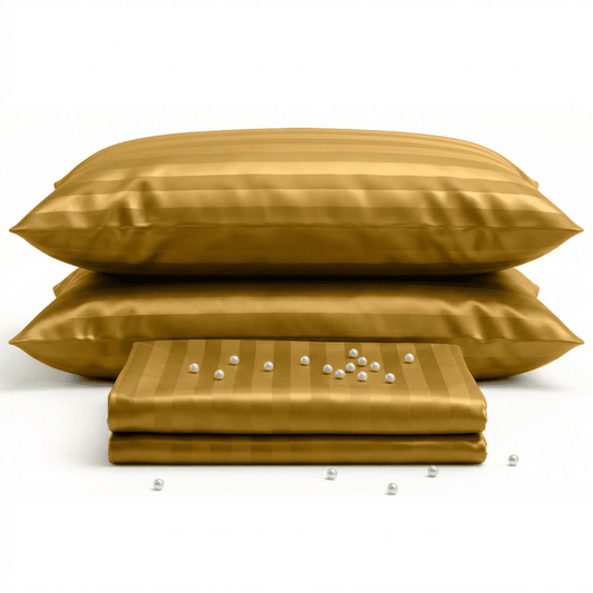 Gold satin pillows and a folded gold satin sheet on a white background
