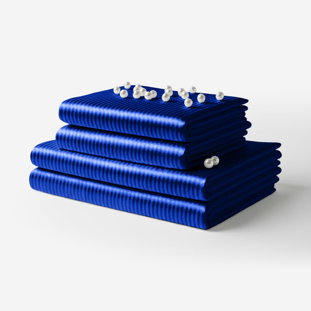 Stack of folded striped blue satin sheets with a smooth, glossy finish and pearl accents on top.