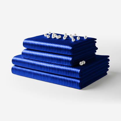 Stack of folded striped blue satin sheets with a smooth, glossy finish and pearl accents on top.