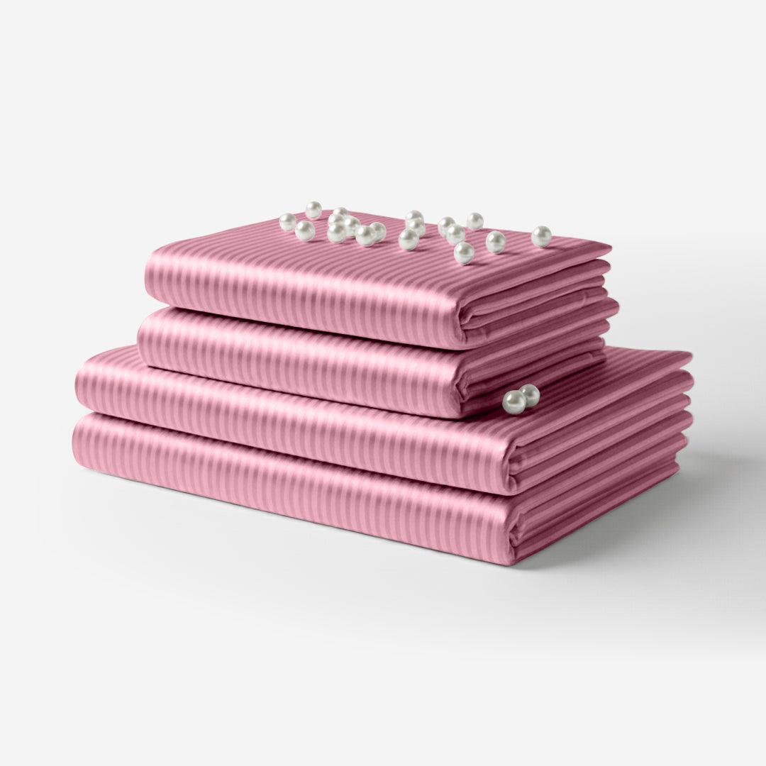 Pink satin sheet set with subtle vertical stripes, neatly folded with small decorative white flowers on top.