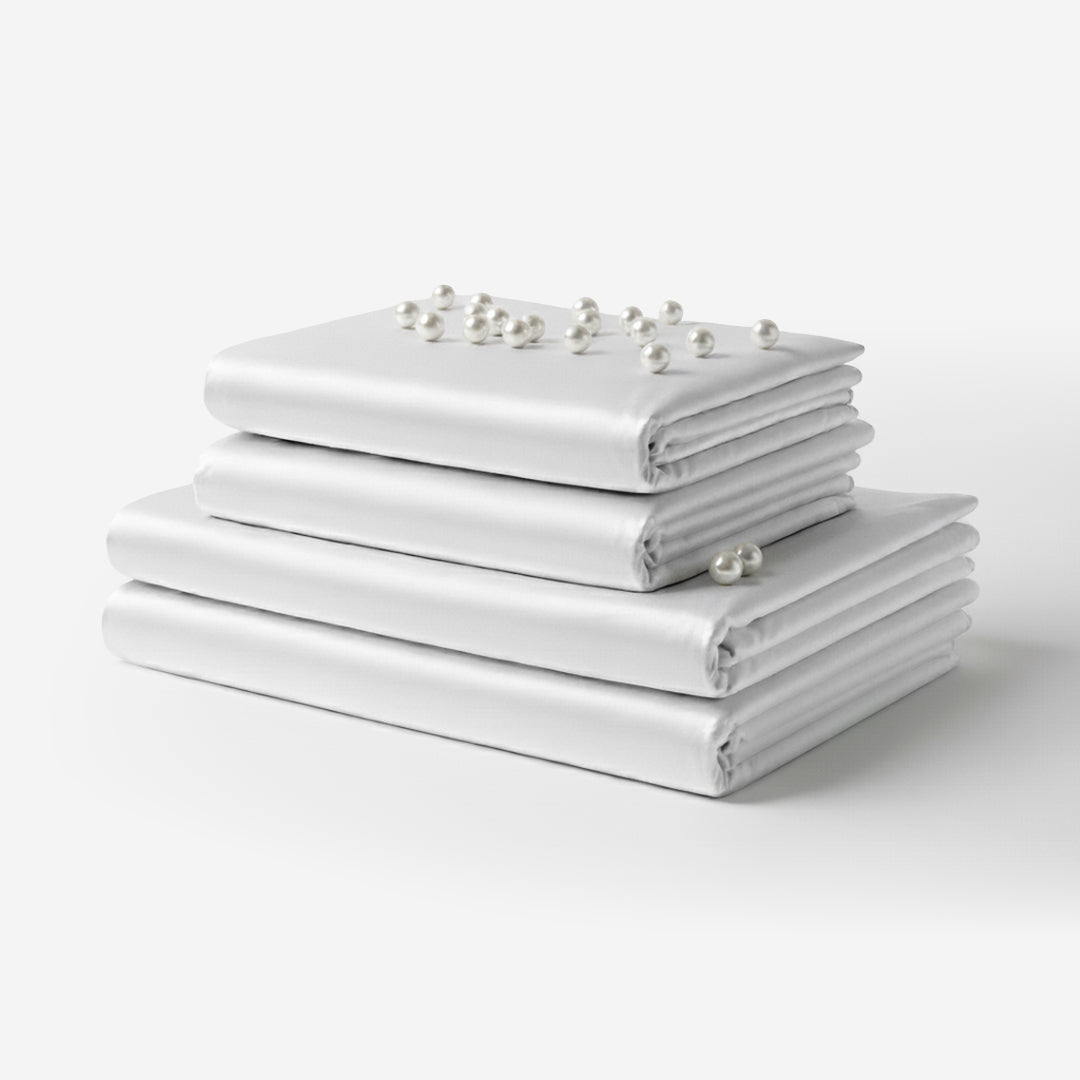 Stack of neatly folded white satin sheets with smooth, glossy finish and pearl accents on top.