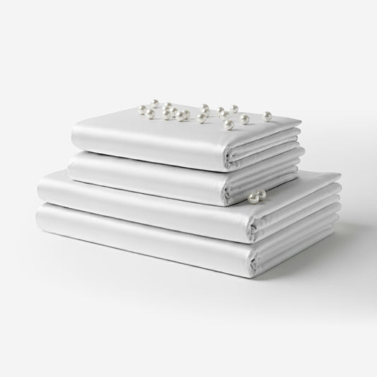 Stack of neatly folded white satin sheets with smooth, glossy finish and pearl accents on top.