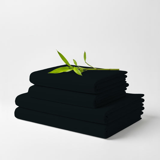 Stack of neatly folded black bamboo bed sheets with green leaf accent on top.