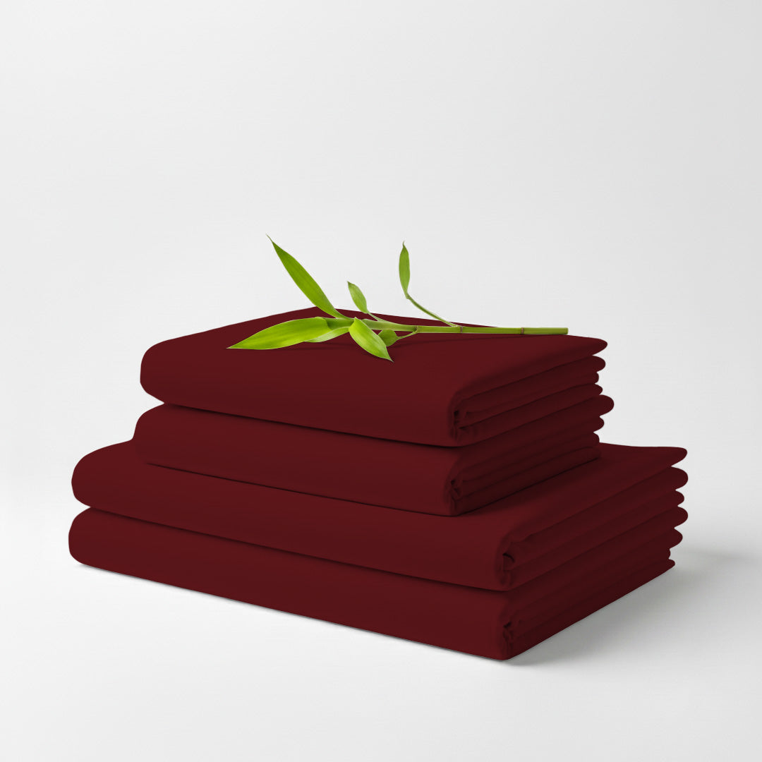 Stack of neatly folded burgundy bamboo bed sheets with a small green leafy twig on top.