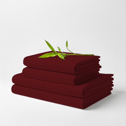 Stack of neatly folded burgundy bamboo bed sheets with a small green leafy twig on top.