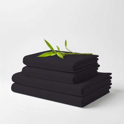 Charcoal bamboo sheet set folded neatly with green leaf accent on top against white background.