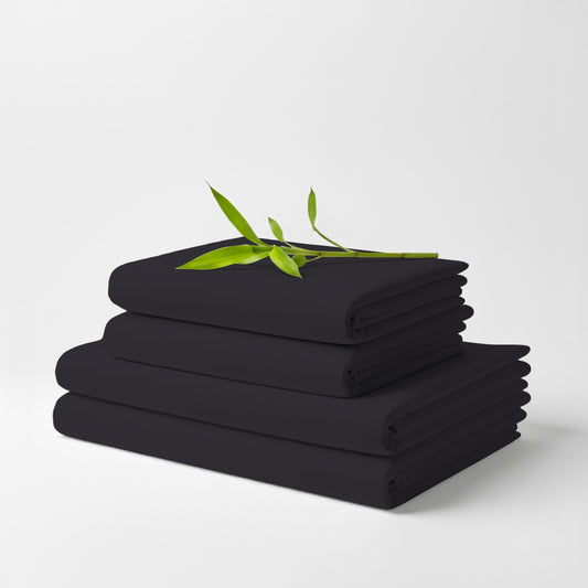 Charcoal bamboo sheet set folded neatly with green leaf accent on top against white background.