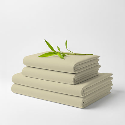 Stack of neatly folded creme bamboo sheets with a small green branch on top against a white background.