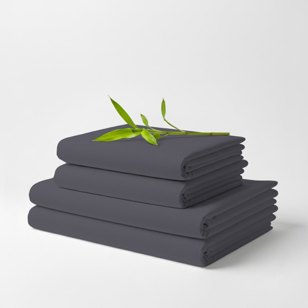 Stack of neatly folded grey bamboo bed sheets with a small green leafy branch on top.