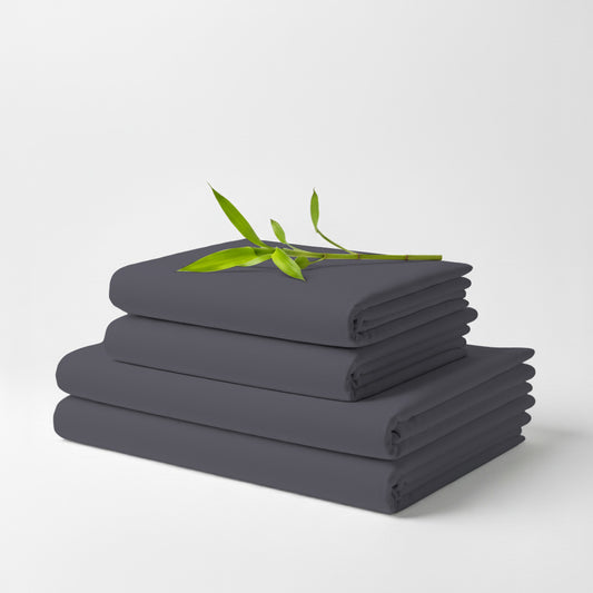 Stack of neatly folded grey bamboo bed sheets with a small green leafy branch on top.