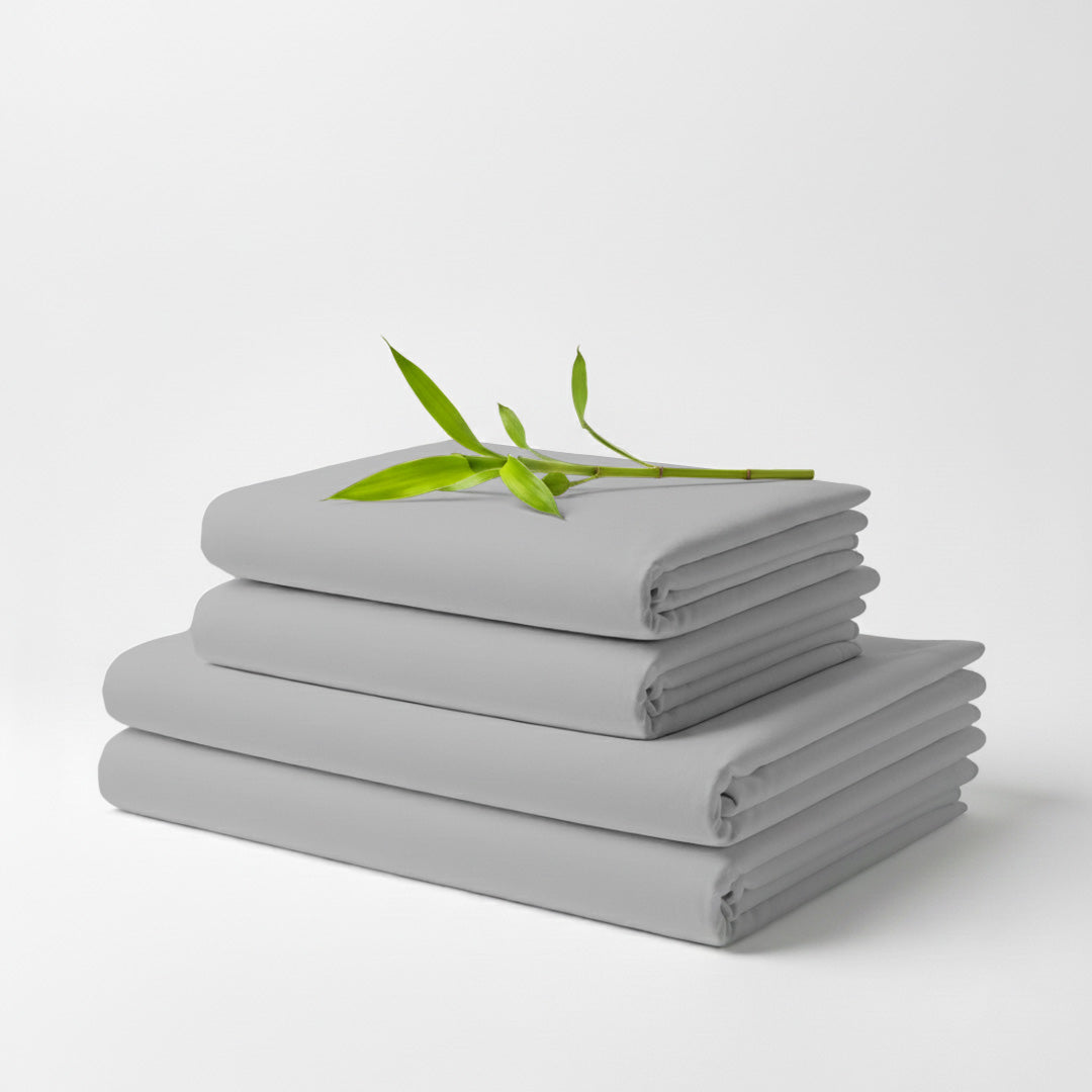 Stack of neatly folded light grey bamboo bed sheets with a small green branch on top.