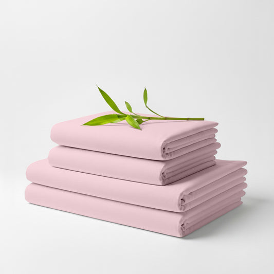 Stack of neatly folded light pink bamboo bed sheets with a small green branch on top.