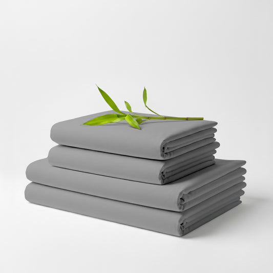 Stack of smooth midgrey bamboo bed sheets folded neatly with a small green plant branch on top.