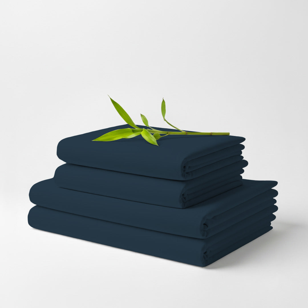 Stack of neatly folded navy blue bamboo sheets with a small green leafy twig on top against a plain white background.
