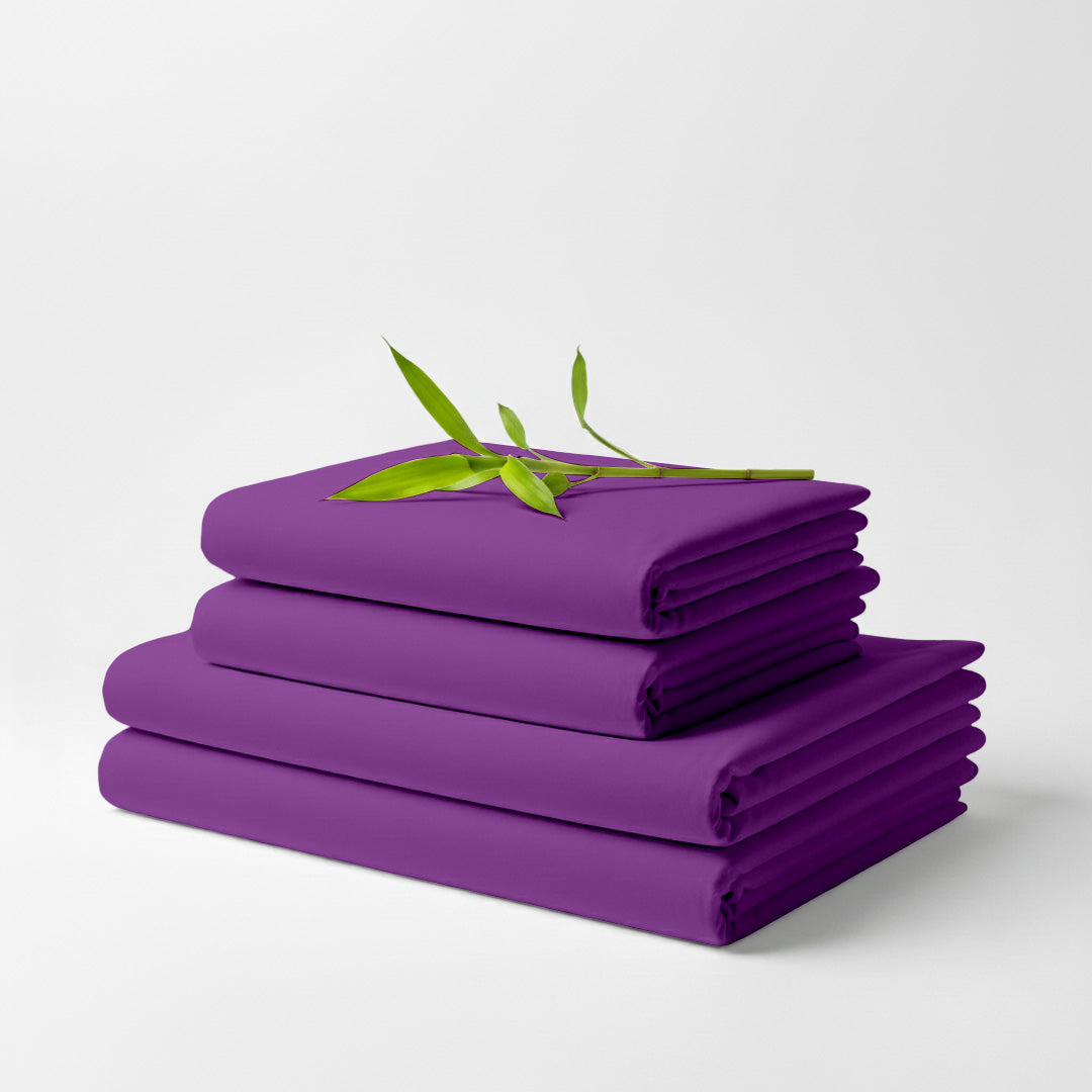 Stack of neatly folded purple bamboo bed sheets with a small green leafy branch on top.