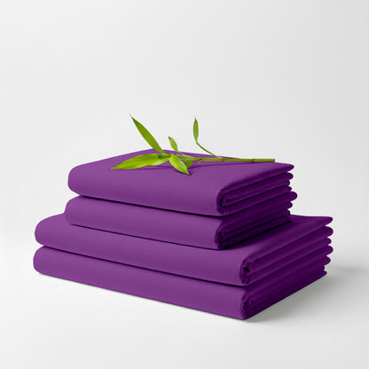 Stack of neatly folded purple bamboo bed sheets with a small green leafy branch on top.