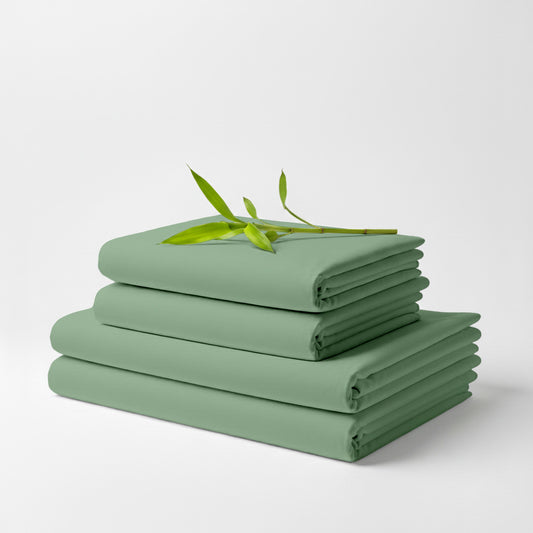Stack of folded sage green bamboo bed sheets with a small green leafy branch on top.