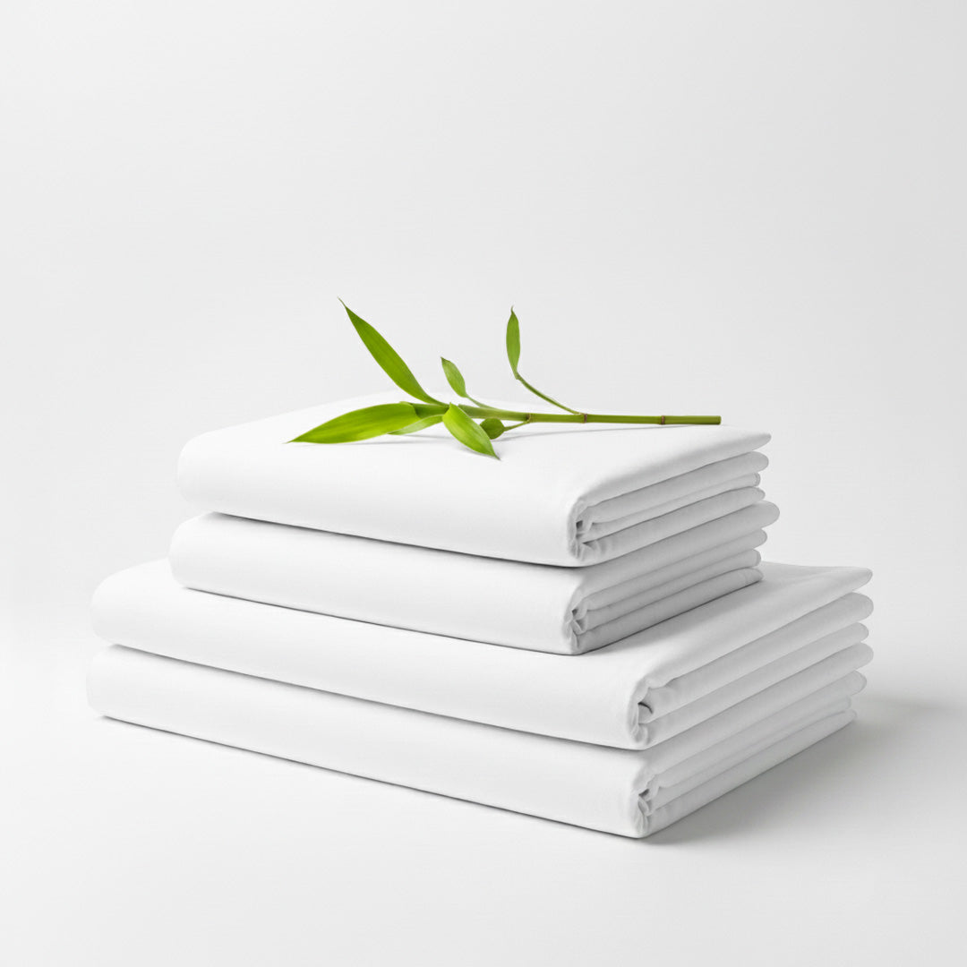 Stack of neatly folded white bamboo bed sheets with a small green leafy twig on top.