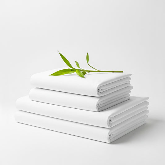 Stack of neatly folded white bamboo bed sheets with a small green leafy twig on top.